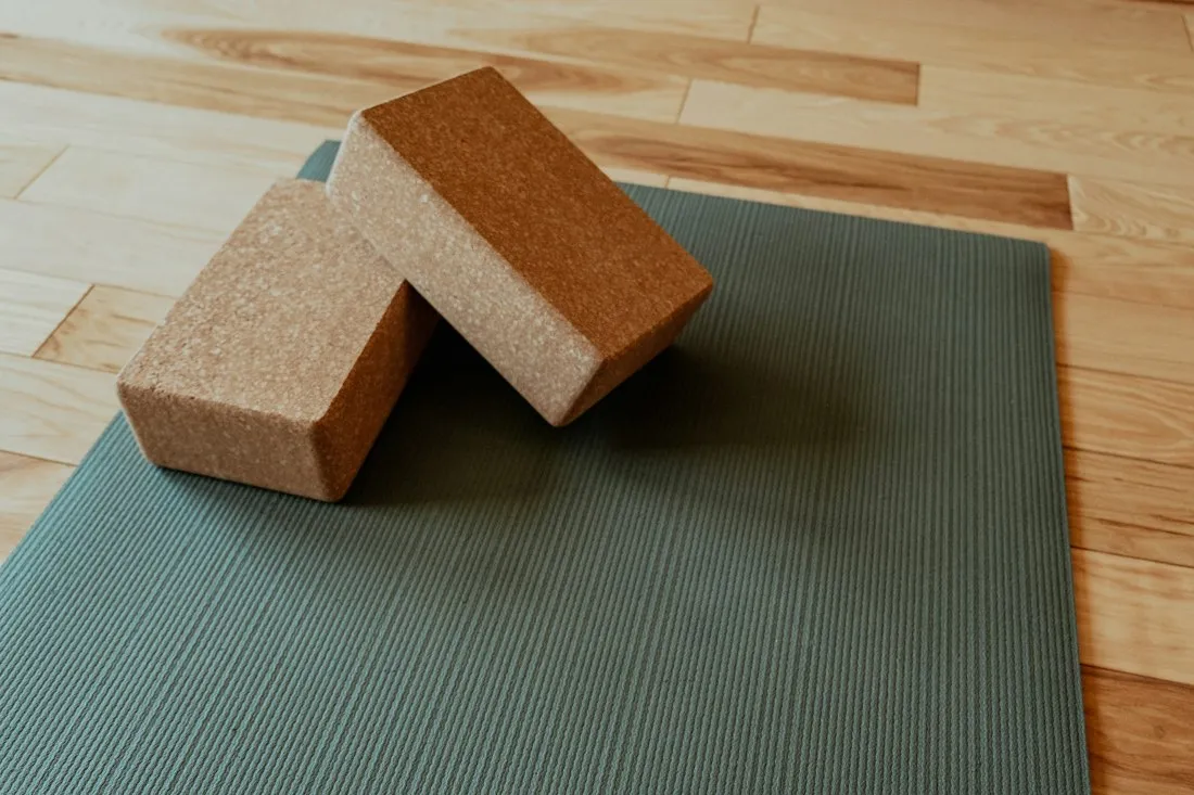 Two cork yoga blocks resting on a sage-green mat on a wooden floor